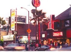 a busy street with cars and people walking on the sidewalk, palm trees in the background