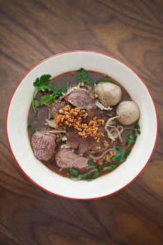 a white bowl filled with meat and veggies on top of a wooden table