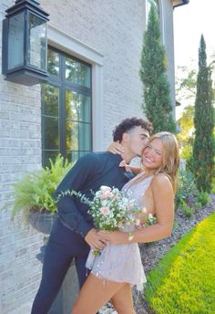 a man and woman are posing for a photo in front of a house with flowers