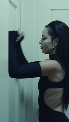 a woman with long black hair is standing in front of a door and holding her arm out