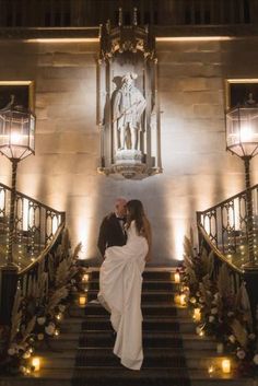 a bride and groom are standing on the stairs in front of an ornate staircase with candles