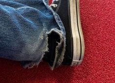 a person's feet with torn jeans and converse shoes on the floor in front of red carpet