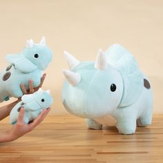 two stuffed rhinoceros are being held up by someone's hand on a wooden floor