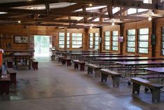 an empty room with tables and benches in the center is full of wood paneled windows