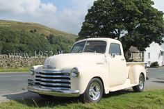 an old white truck is parked on the side of the road in front of a house