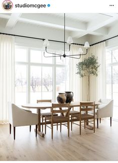 a dining room table with chairs and a vase on top of it in front of large windows