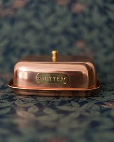 a golden butter dish sitting on top of a blue and green tablecloth covered surface