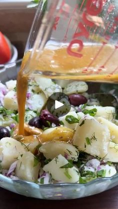 a glass bowl filled with potato salad and dressing being poured over it's side