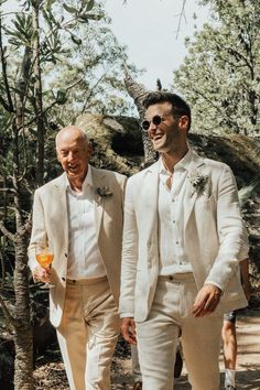 two men in white suits walking down a path together, one is wearing sunglasses and the other has a flower on his head