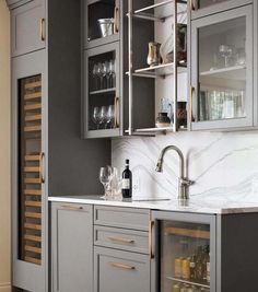 a kitchen with gray cabinets and white marble counter tops, wine glasses on the shelves