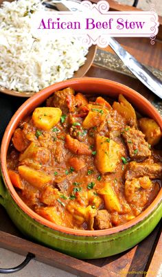 an african beef stew in a bowl with rice and spoons on the side next to it