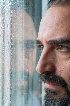 a man with a beard looking out the window