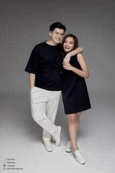 a man and woman are posing for a photo together in front of a gray background