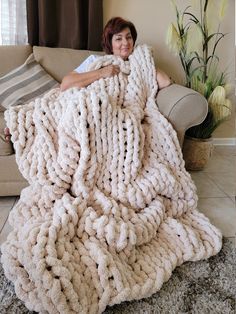 a woman sitting on top of a couch under a giant chunky knitted blanket