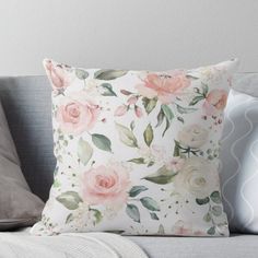 a white pillow with pink flowers and green leaves on the front is sitting on a gray couch