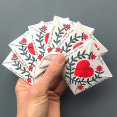 a hand holding four folded cards with red and green designs on them, all in the shape of hearts