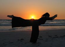 a woman standing on top of a sandy beach next to the ocean at sun set