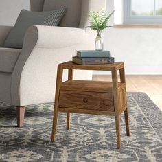 a small wooden end table with two books on it and a plant in a vase