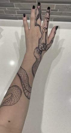 a woman's hand with a snake tattoo on her left arm and black nails