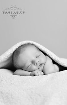 a black and white photo of a sleeping baby wrapped in a blanket with his eyes closed