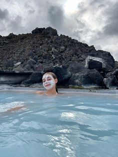 a woman in the water with facial mask on her face and some rocks behind her