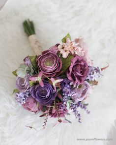 a bridal bouquet with purple flowers and greenery on a white furnishing