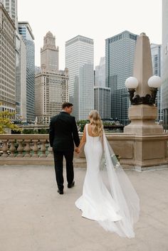 a bride and groom holding hands while walking in front of the city skyline with skyscrapers