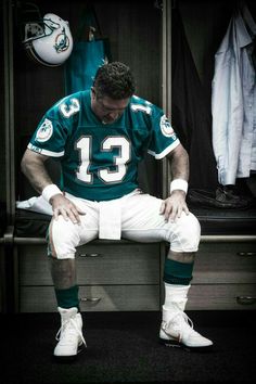 a man sitting on top of a wooden bench in a dressing room wearing a football uniform