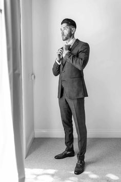 a man standing in front of a mirror wearing a suit and looking at his tie