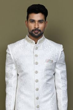 Off white full sleeves sherwani crafted in imported jacquard silk with all over bloom pattern and hand embroidery on the band collar neckline and buttons. Paired with an off white dupion art silk Aligadhi pant. - Aza Fashions White Brocade Kurta For Diwali, White Bandhgala For Groom With Pallu Detail, White Bandhgala With Pallu For Groom, Festive White Brocade Kurta, White Brocade Bandhgala For Eid, White Brocade Bandhgala For Festive Occasions, Festive White Brocade Bandhgala, White Brocade Kurta With Pallu Detail, White Brocade Traditional Wear With Chikankari Embroidery