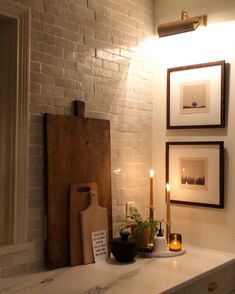 a white brick wall with candles and pictures hanging on it's side, next to a counter