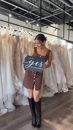 a woman holding a sign that says yes in front of wedding dresses hanging on racks