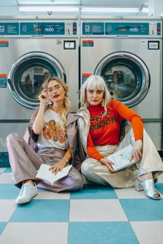 two women sitting next to each other in front of washers and dryer machines