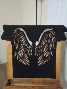 a black shirt with white wings on it sitting on a wooden stand in front of a wall