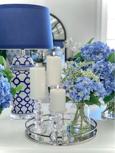 blue and white vases with flowers in them on a glass tray next to a lamp