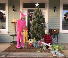 two people dressed up in costumes standing next to a christmas tree with presents on the ground