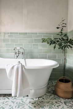 a white bath tub sitting next to a potted plant on top of a tiled floor