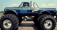 a large blue truck with huge tires on it's flatbed in the dirt