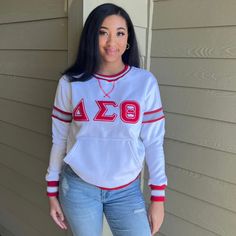 a woman standing in front of a house wearing a white sweater with red letters on it