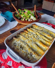 a casserole dish with cheese and vegetables on the side next to a bowl of salad