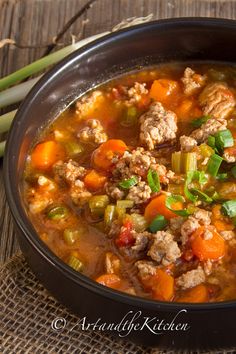 a close up of a bowl of soup with meat and vegetables on a wooden table