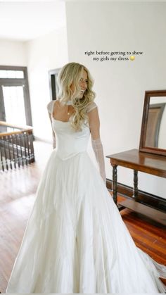 a woman in a white wedding dress standing on a wooden floor next to a mirror