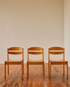 two wooden chairs sitting next to each other on top of a hard wood floor in front of a white wall