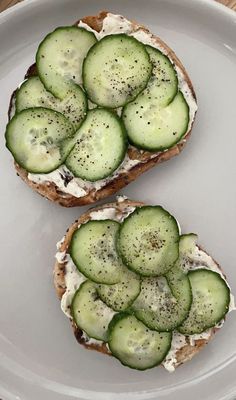 two pieces of bread with cucumbers on them sitting on a plate next to each other