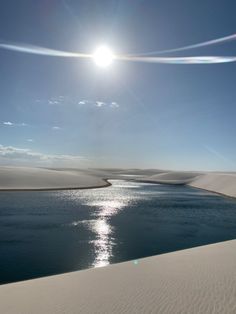 the sun shines brightly over an expanse of sand dunes and water in the foreground