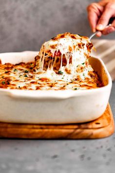 a person holding a fork in a casserole dish with cheese and sauce on top