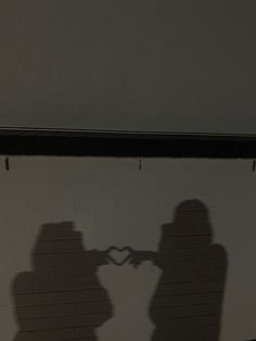 the shadow of two people making a heart with their hands on a white brick wall