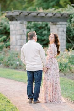 an engaged couple holding hands and walking down a path in front of some flowers at the park