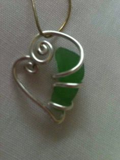 a heart shaped pendant with green sea glass in the shape of a wire wrapped around it