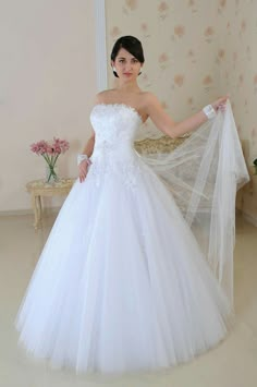 a woman in a white wedding dress holding her veil over her shoulder and posing for the camera